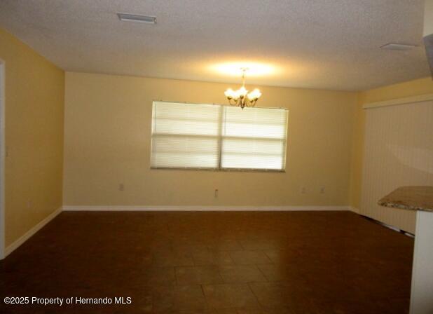 spare room featuring a chandelier, visible vents, a textured ceiling, and baseboards