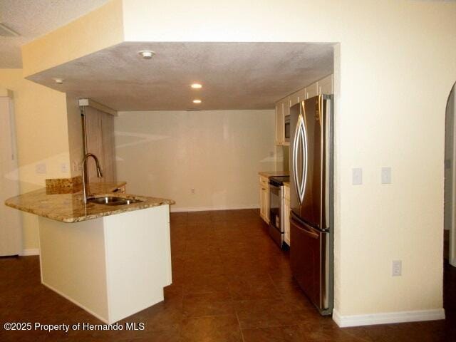 kitchen featuring arched walkways, electric stove, freestanding refrigerator, a sink, and a peninsula