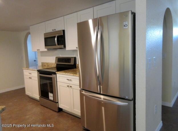 kitchen featuring arched walkways, appliances with stainless steel finishes, white cabinetry, and baseboards