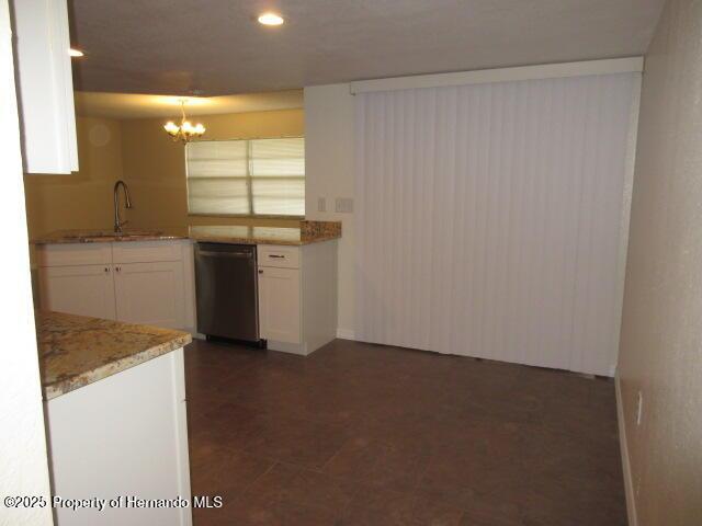 kitchen with light stone counters, white cabinetry, a sink, a chandelier, and dishwashing machine