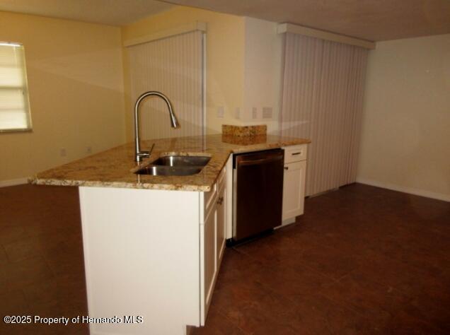 kitchen with dishwashing machine, light stone counters, a peninsula, white cabinetry, and a sink