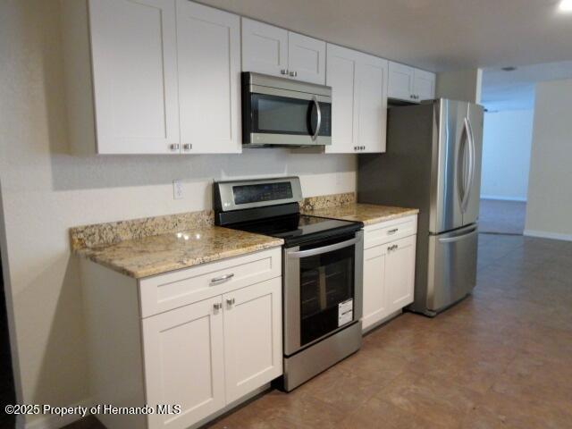 kitchen with stainless steel appliances, light stone counters, and white cabinetry