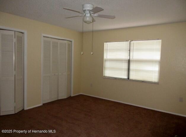 unfurnished bedroom with a ceiling fan, carpet flooring, baseboards, and two closets