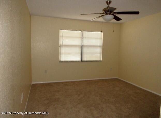 carpeted spare room with ceiling fan and baseboards