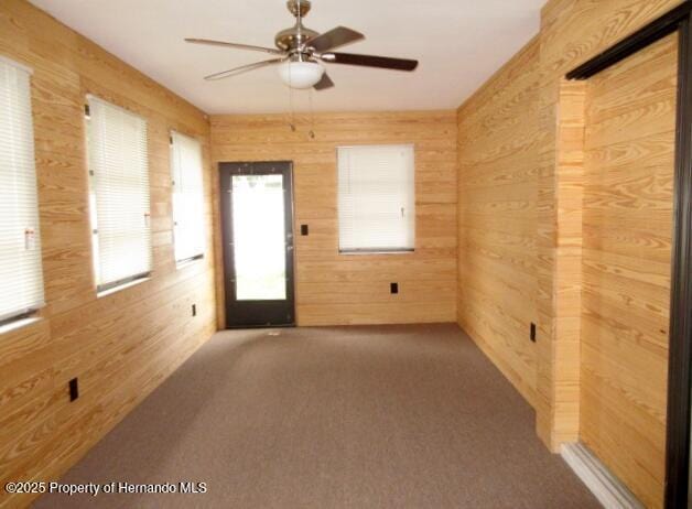 carpeted spare room with a ceiling fan and wood walls