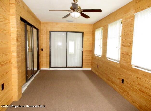 carpeted empty room with ceiling fan and wooden walls