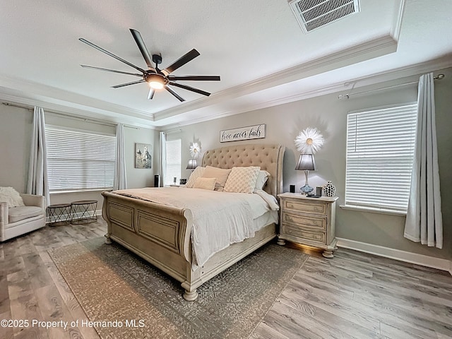 bedroom with light wood finished floors, visible vents, ornamental molding, a tray ceiling, and multiple windows