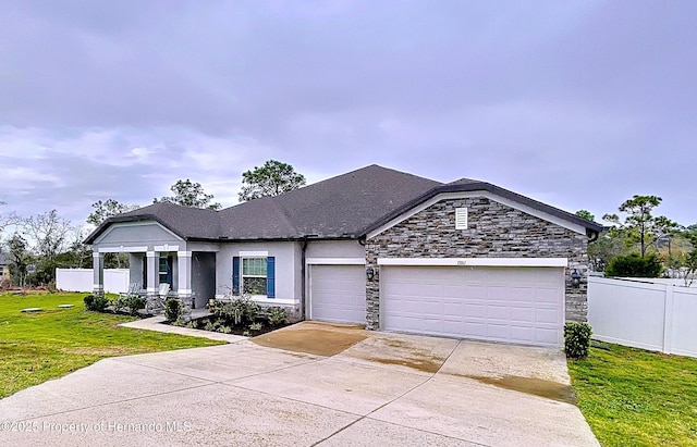 view of front of house with driveway, stone siding, an attached garage, fence, and a front lawn