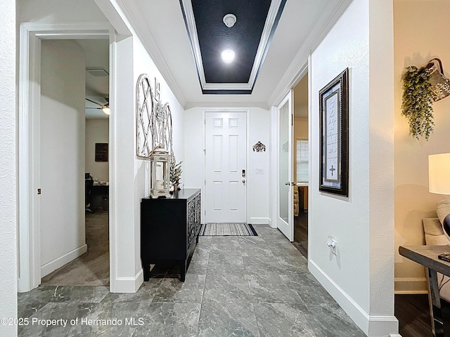 entrance foyer featuring ornamental molding, a raised ceiling, and baseboards