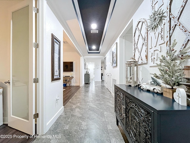 hall featuring a raised ceiling, visible vents, crown molding, and baseboards