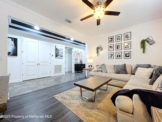 living area with a ceiling fan, wood finished floors, visible vents, and crown molding