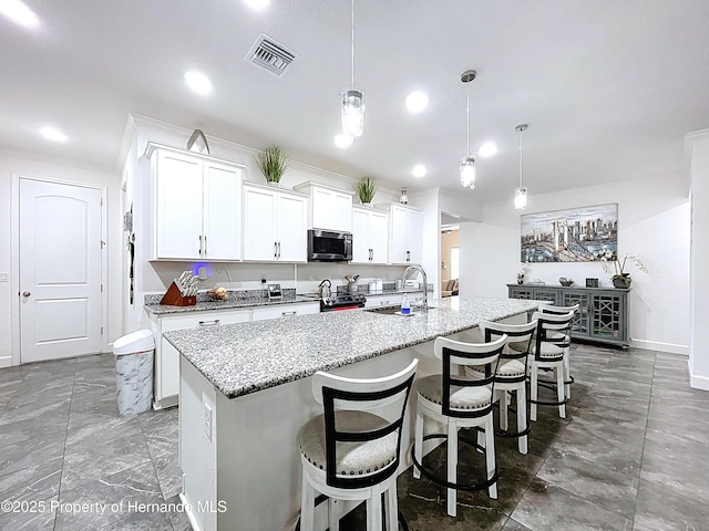 kitchen featuring a sink, visible vents, electric range oven, stainless steel microwave, and a center island with sink