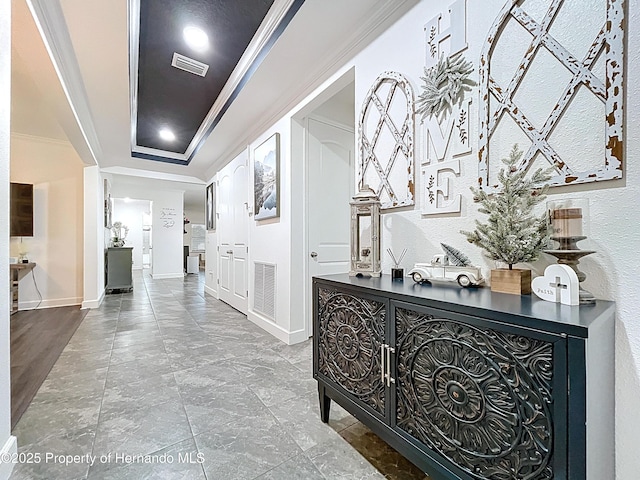 hallway featuring visible vents, ornamental molding, a raised ceiling, and baseboards