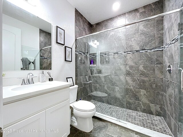 full bathroom with a textured wall, toilet, a tile shower, a textured ceiling, and vanity