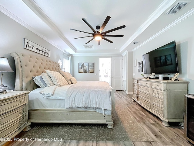 bedroom with crown molding, visible vents, a raised ceiling, and wood finished floors