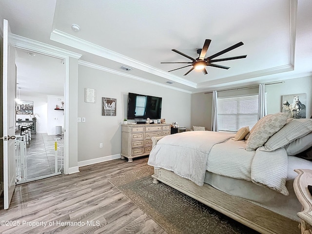 bedroom featuring light wood finished floors, baseboards, visible vents, a tray ceiling, and crown molding