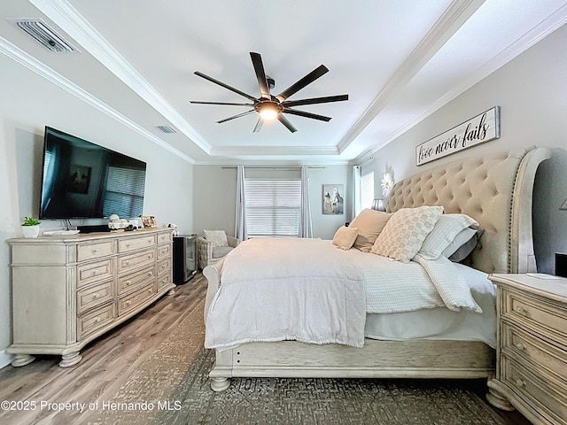 bedroom with a raised ceiling, visible vents, crown molding, and wood finished floors