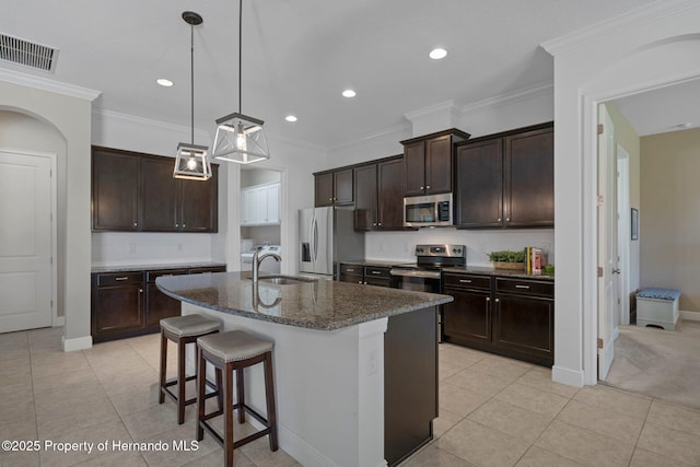 kitchen featuring stainless steel appliances, a sink, visible vents, a kitchen breakfast bar, and dark stone countertops