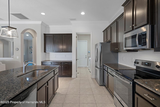 kitchen featuring dark brown cabinetry, appliances with stainless steel finishes, dark stone countertops, a sink, and light tile patterned flooring