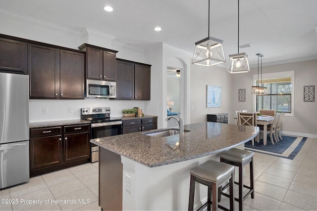 kitchen featuring light tile patterned floors, arched walkways, dark stone counters, stainless steel appliances, and a sink