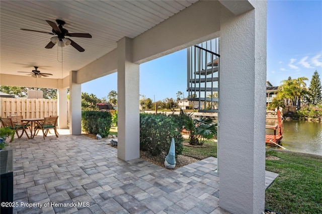 view of patio / terrace with outdoor dining area, a water view, fence, a ceiling fan, and stairway