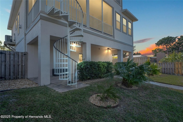 back of property at dusk featuring stucco siding, a lawn, fence, and stairs