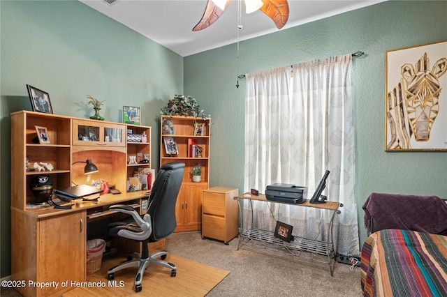 office space featuring a textured wall, ceiling fan, and light colored carpet