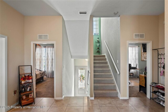 tiled foyer featuring stairway, visible vents, and baseboards