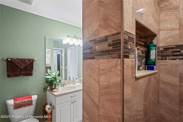 bathroom with visible vents, a textured wall, vanity, and toilet