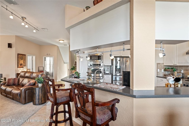 kitchen with tasteful backsplash, dark countertops, appliances with stainless steel finishes, open floor plan, and a breakfast bar area