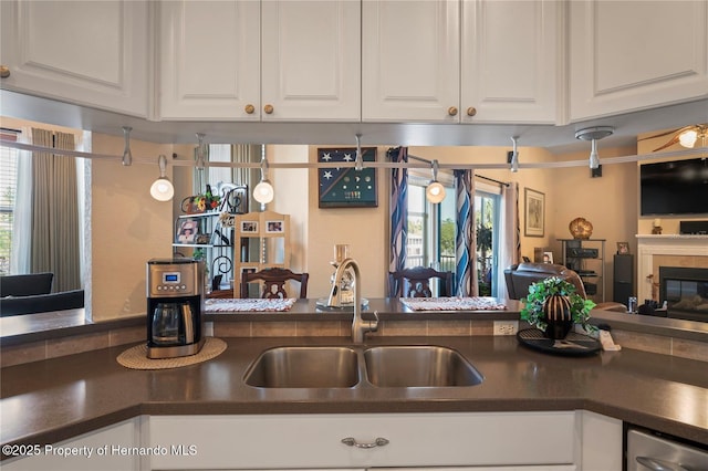 kitchen with dark countertops, white cabinetry, open floor plan, and a sink