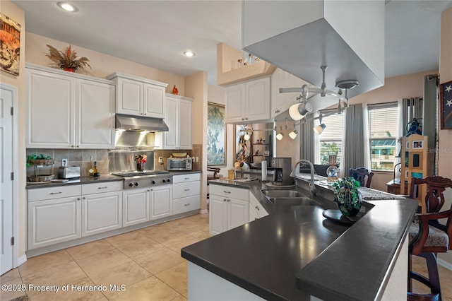 kitchen featuring under cabinet range hood, stainless steel gas cooktop, a sink, white cabinets, and dark countertops