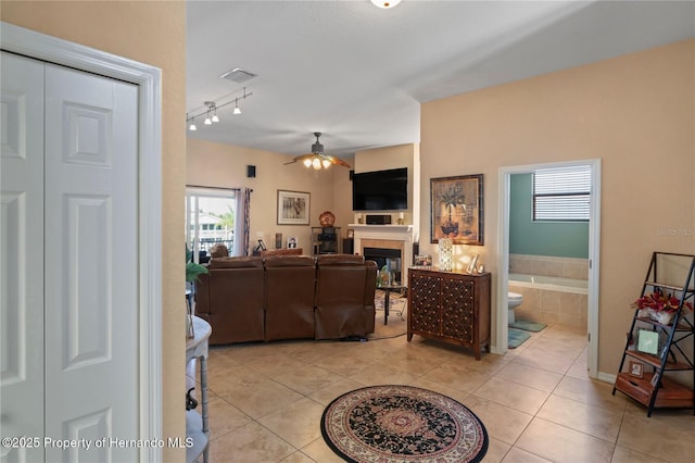 living area featuring ceiling fan, light tile patterned flooring, a glass covered fireplace, and visible vents