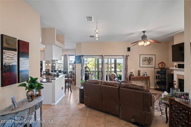 living area with light tile patterned flooring, visible vents, a fireplace, and ceiling fan