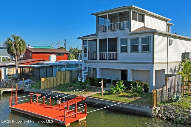 rear view of house featuring a sunroom, a water view, fence, and stairs