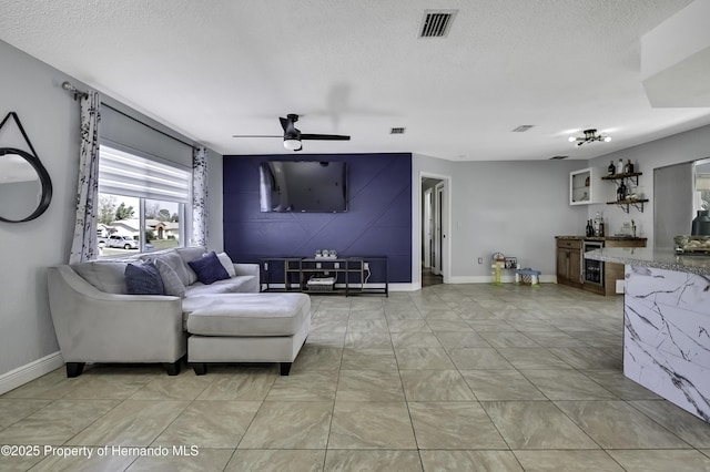 living room featuring a textured ceiling, wine cooler, visible vents, and a ceiling fan