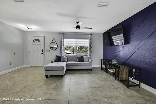 living area with baseboards, ceiling fan, visible vents, and a textured ceiling