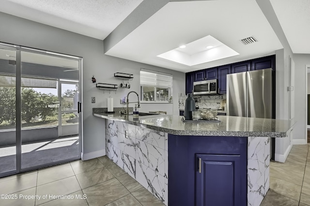 kitchen with a peninsula, a sink, visible vents, appliances with stainless steel finishes, and blue cabinetry