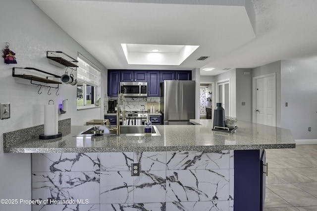 kitchen with a tray ceiling, blue cabinetry, stainless steel appliances, visible vents, and a peninsula