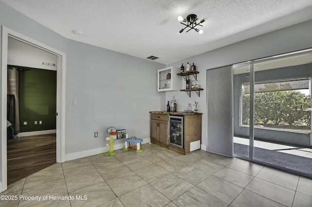 bar with light tile patterned floors, visible vents, wine cooler, wet bar, and a textured ceiling