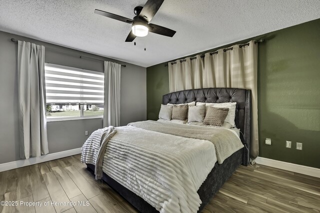 bedroom featuring a ceiling fan, a textured ceiling, baseboards, and wood finished floors