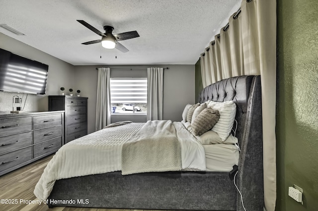 bedroom with a ceiling fan, a textured ceiling, visible vents, and wood finished floors