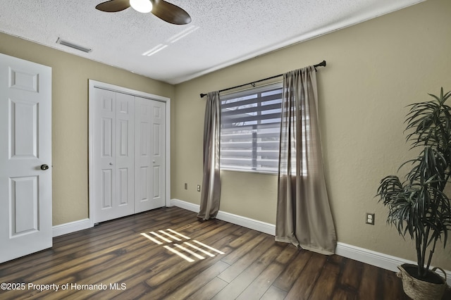 unfurnished bedroom with dark wood finished floors, a closet, visible vents, a textured ceiling, and baseboards