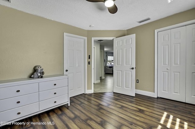 unfurnished bedroom featuring a textured ceiling, ceiling fan, dark wood-style flooring, visible vents, and a closet