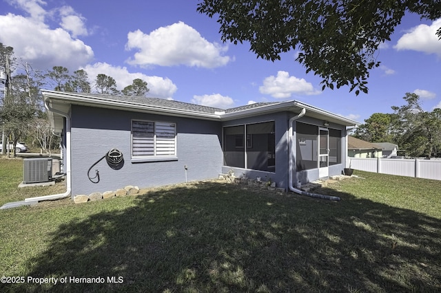 rear view of house featuring stucco siding, central air condition unit, a lawn, a sunroom, and fence