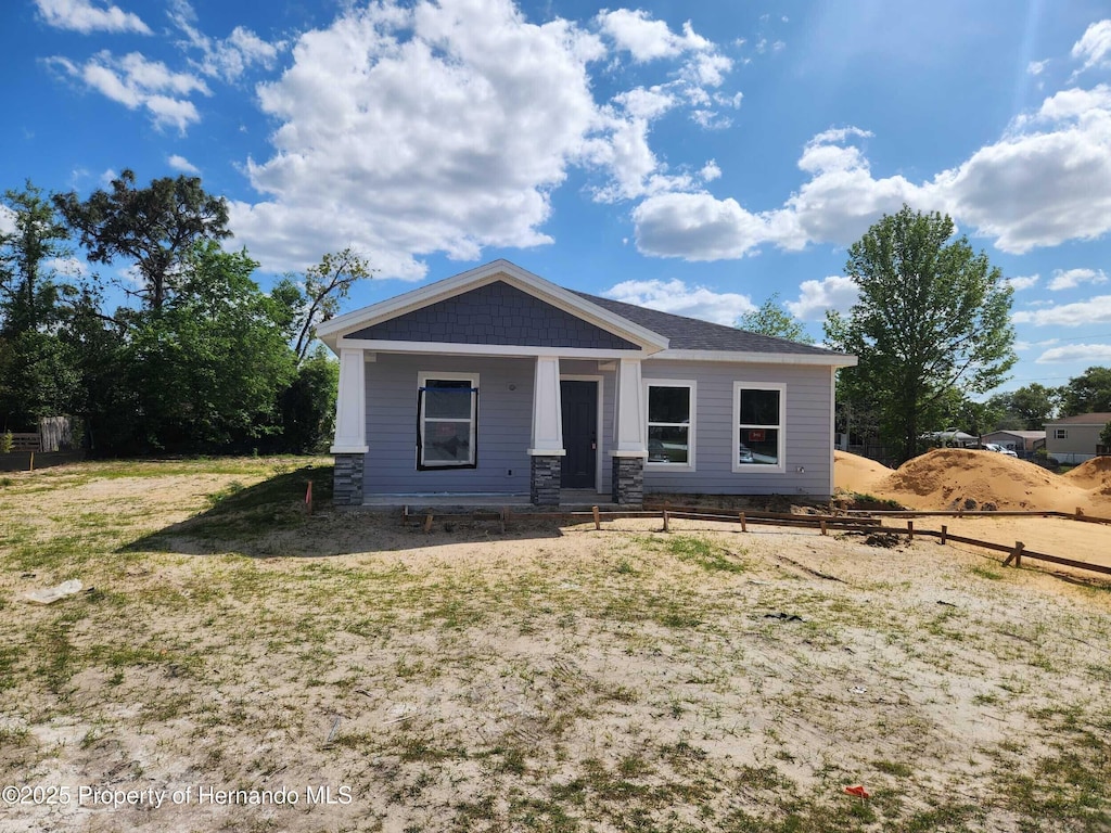 bungalow-style home with fence, stone siding, and covered porch