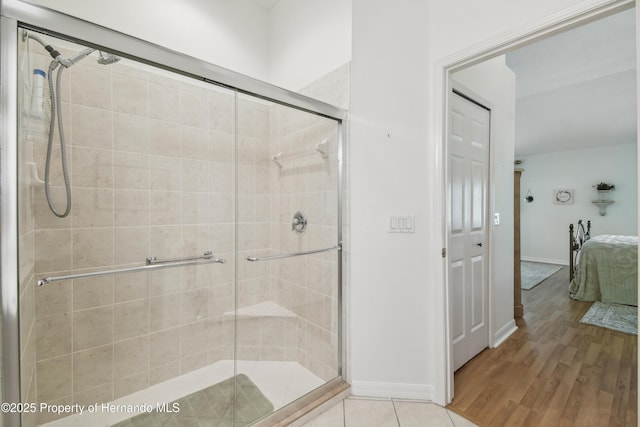 bathroom featuring wood finished floors, a stall shower, ensuite bath, and baseboards