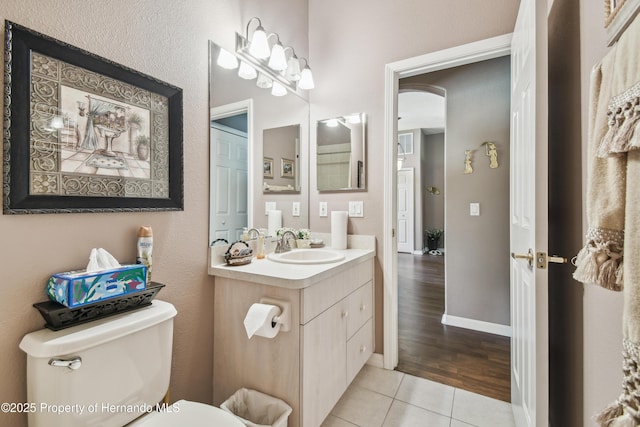 half bath featuring baseboards, vanity, toilet, and tile patterned floors