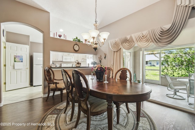 dining room with a chandelier, arched walkways, and light wood finished floors