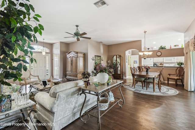 living area featuring baseboards, visible vents, arched walkways, dark wood-style flooring, and ceiling fan with notable chandelier